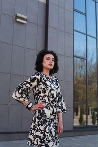 Fashionable young woman wearing floral patterned dress standing against building in city