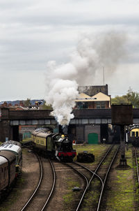 Steam train emitting smoke at shunting yard against sky