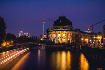 Illuminated bridge over river by buildings in city at night