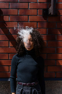 Portrait of young woman standing against brick wall