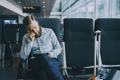 Businessman using digital tablet while sitting in waiting room at airport departure area