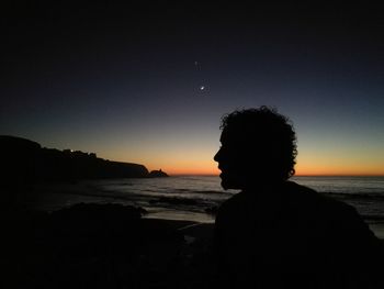 Silhouette boy standing at beach against sky during sunset