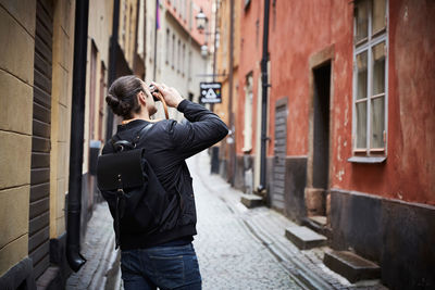 Rear view of man photographing through camera while standing in alley