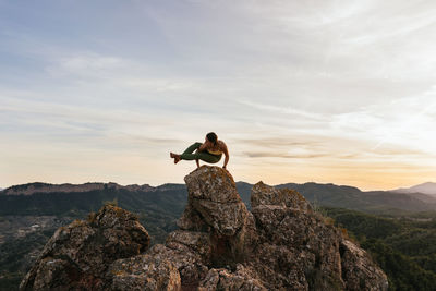 Confident young female performing eight angle posture on top of rocky mountain on height