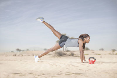 Full length of woman exercising in desert against sky