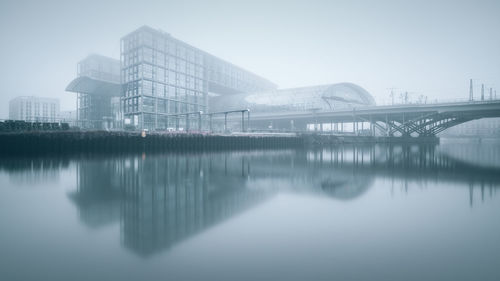 Berlin hauptbahnhof with reflection on river against sky in foggy weather