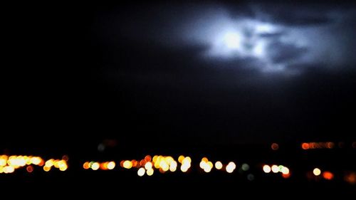 Defocused image of illuminated lights against sky at night