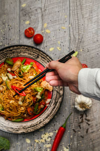 Cropped hand of man holding chopsticks over food on table