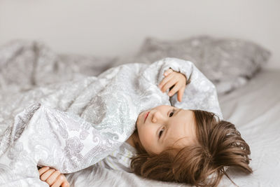 An adorable little boy plays around on the bed and wraps himself in a blanket. 