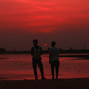 Silhouette couple standing on street against orange sky