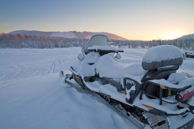 Snow covered field and snowmobile  against sky during sunset