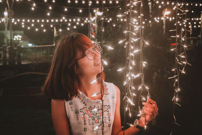 Smiling young woman wearing eyeglasses looking illuminated lights at night