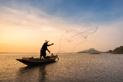 Fisherman fishing against cloudy sky during sunset