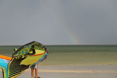 Man holding umbrella on beach against sky