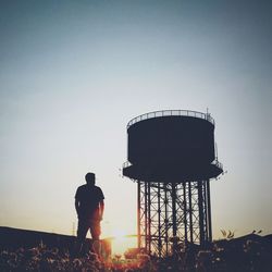 Low angle view of silhouette man standing by water tower against clear sky