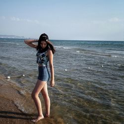 Full length portrait of young woman standing on beach against sky