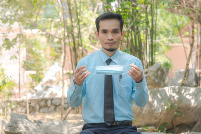 Portrait of young man holding camera while standing on land