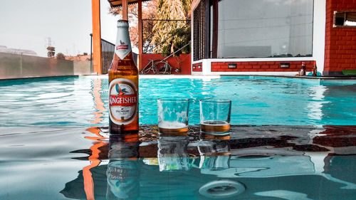 Glass of water on table by swimming pool against buildings