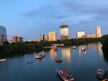 Boats in river by buildings in city against sky