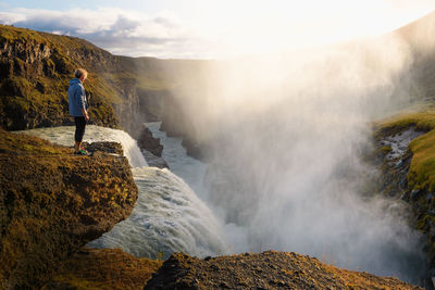 Rear view of man standing on rock against waterfall