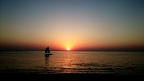 Silhouette boat sailing in sea against sky during sunset