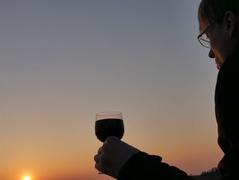 Close-up of man drinking red wine against sky during sunset