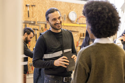 Smiling male worker holding electronic device while talking to customer at recycling center