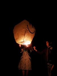 People standing by illuminated lantern against sky at night