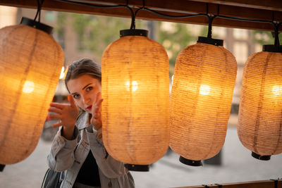 Portrait of young woman seen through illuminated lanterns while standing outdoors
