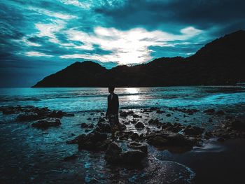 Man standing on rock by sea against sky