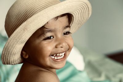 Close-up of smiling boy wearing hat siting on bed at home