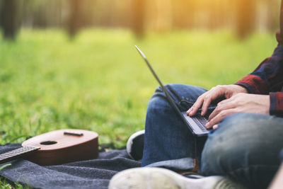 Midsection of man using mobile phone in grass