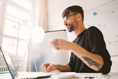 Low angle view of tattooed young man working at desk in office