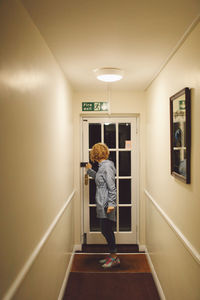 Side view of young woman opening door in illuminated building