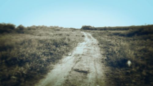 Road amidst field against clear sky