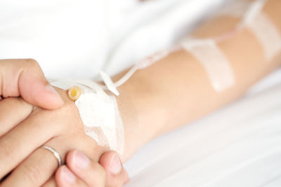 Close-up of doctor holding patient hand on bed at hospital