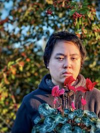 Young asian man with red flowering cyclamen plant against orange rowan berry trees.