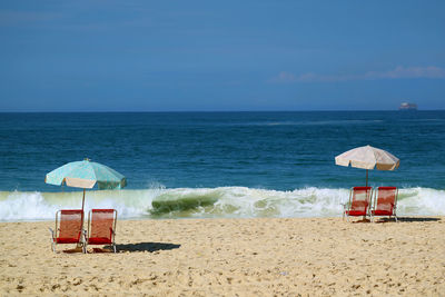 Deck chairs on beach by sea against sky