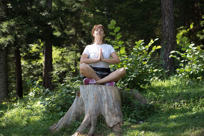 Full length of young woman doing yoga on tree stump at forest