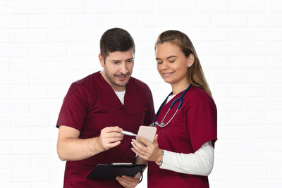 Smiling young woman using phone while standing on wall