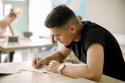 Teenage boy studying while sitting by table in classroom