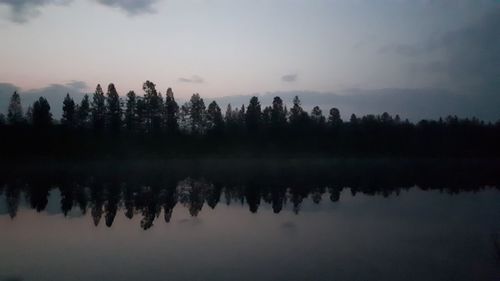 Reflection of silhouette trees in lake against sky at sunset