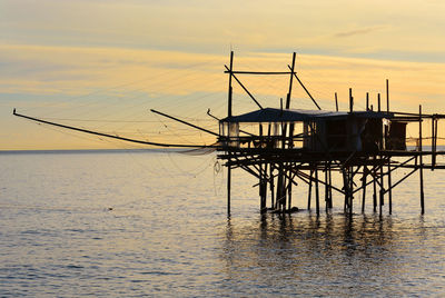 Silhouette fishing net on sea against sky during sunset