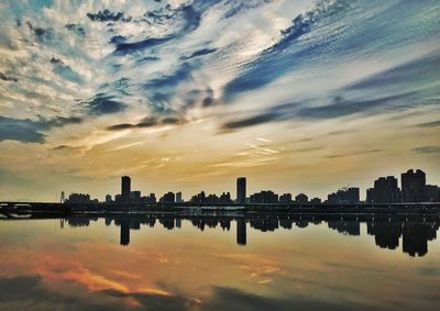 Scenic view of lake by buildings against sky during sunset