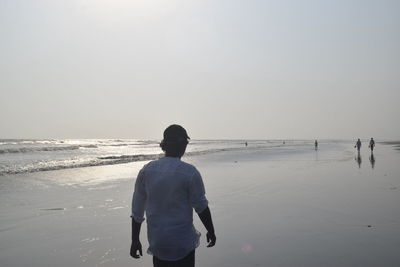 Rear view of man walking on beach against clear sky