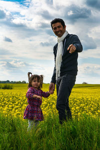 Portrait of father and daughter standing on field against cloudy sky