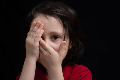 Close-up portrait of boy covering face against black background