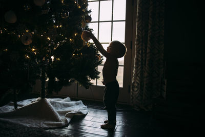 Side view of boy decorating christmas tree while standing at home