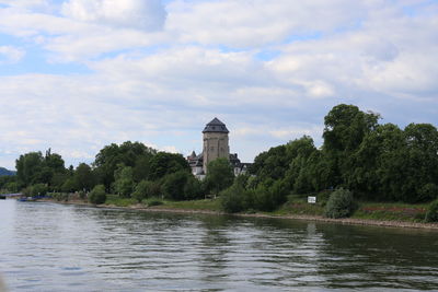 View of buildings at riverbank against cloudy sky