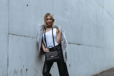 Portrait of young woman standing against wall